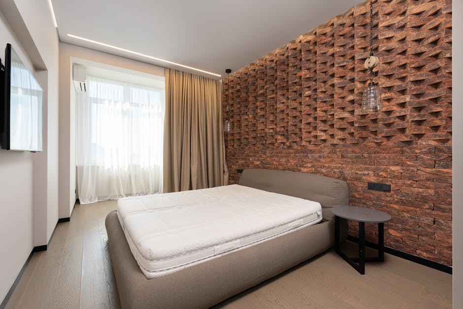 Comfortable bed with mattress placed against modern TV and decorative wall in stylish bedroom with curtains on window at home