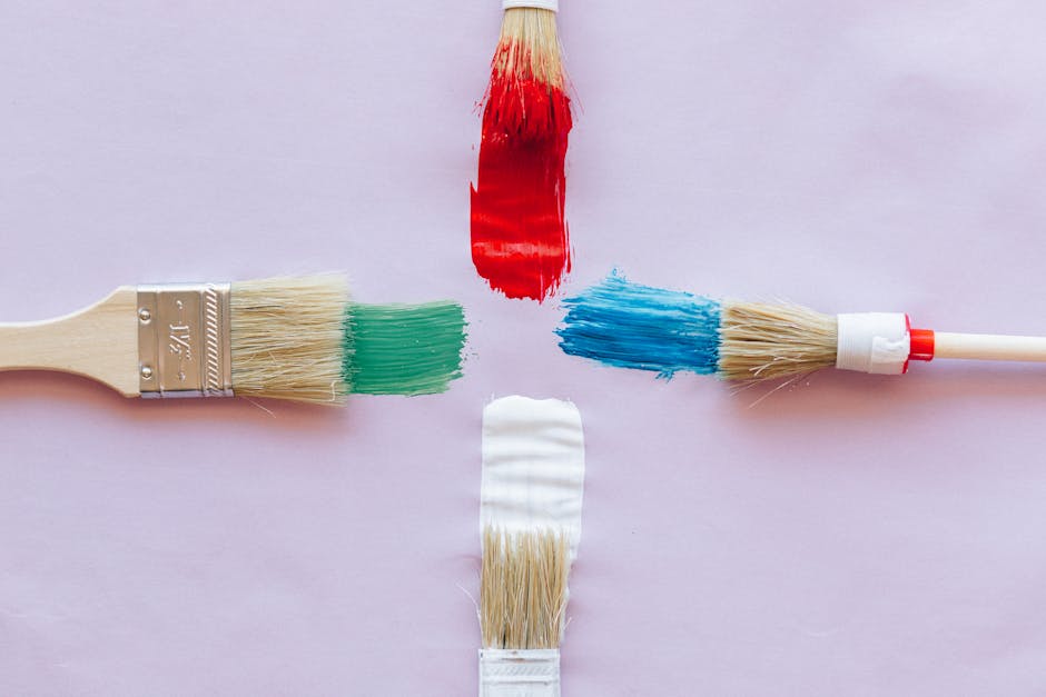 Four paint brushes with vibrant red, green, blue, and white strokes on pastel backdrop.