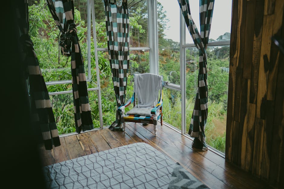 A cozy room with a colorful chair, checkered curtains, and a lush green view through large windows.