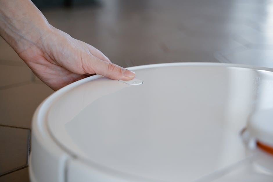 Close-up of a hand pressing a button on a robotic vacuum cleaner indoors.