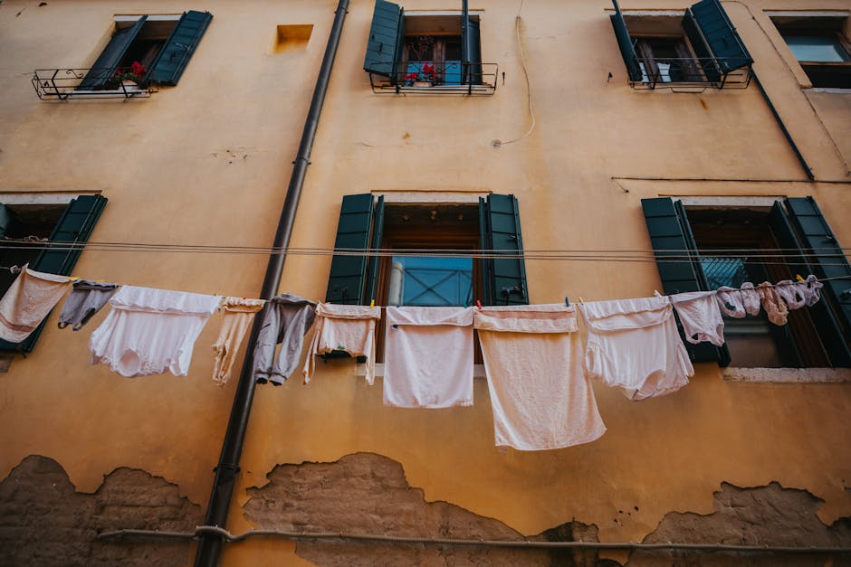 Laundry drying on a clothesline in front of a rustic Italian apartment building with green shutters.