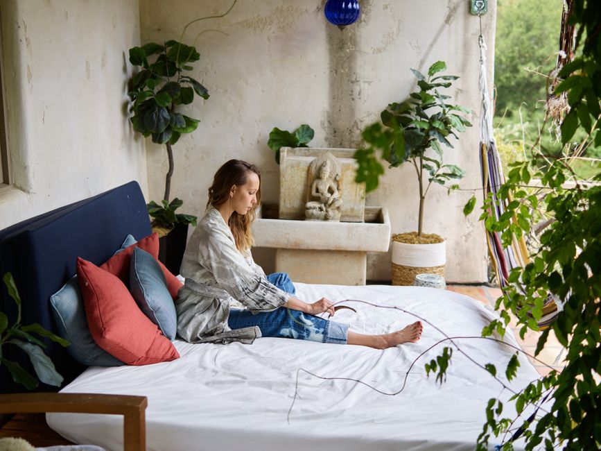 A woman relaxes in a cozy bedroom adorned with plants and elegant decor.