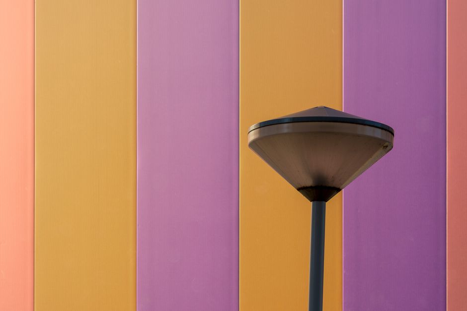 A modern lamp post against a vibrant wall with colorful stripes.