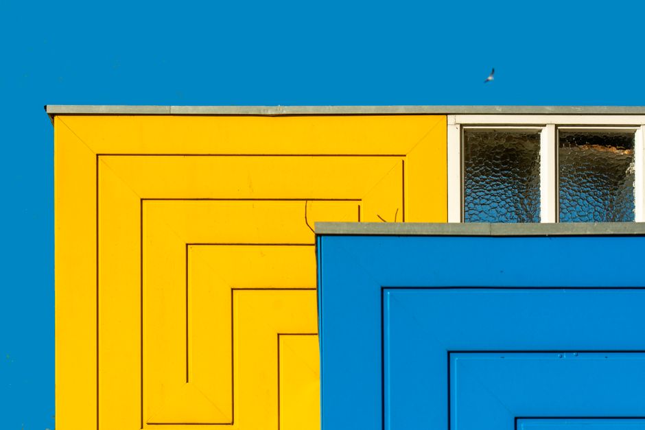 Vibrant architectural detail of a building facade featuring yellow and blue geometric patterns with clear blue sky.