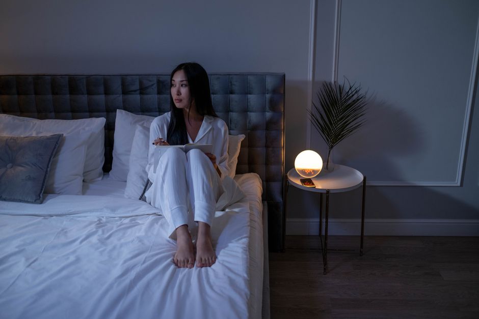 A woman in pajamas sits on a bed in a dimly lit bedroom, creating a serene nighttime atmosphere.