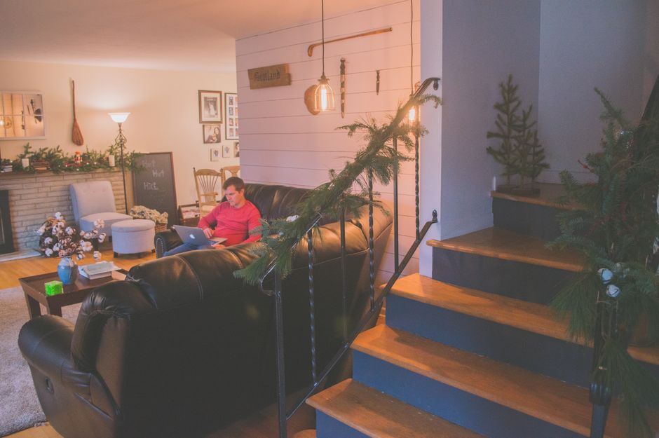A cozy living room adorned with holiday decor, featuring a person working remotely on a laptop.