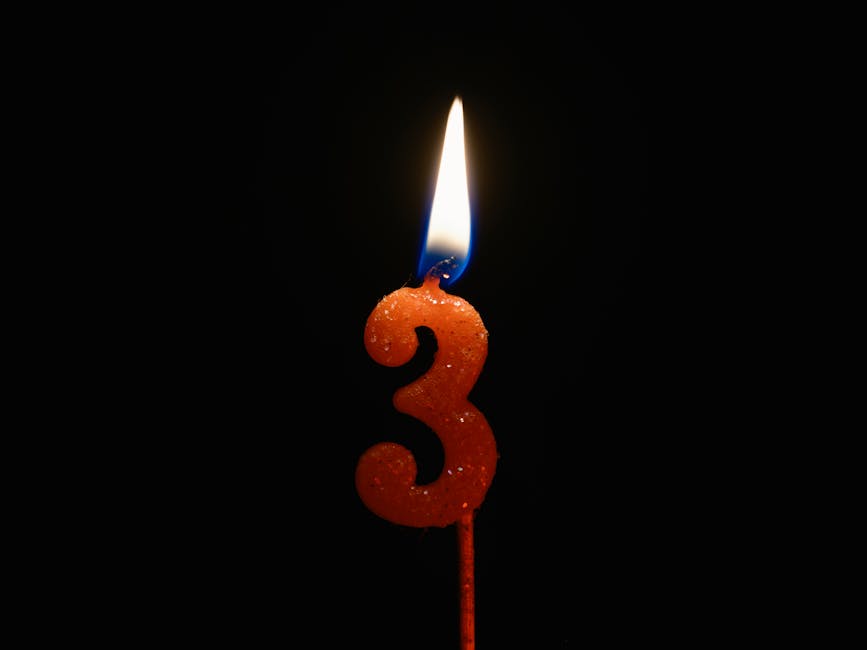 Candle in shape of number three burning against black background.