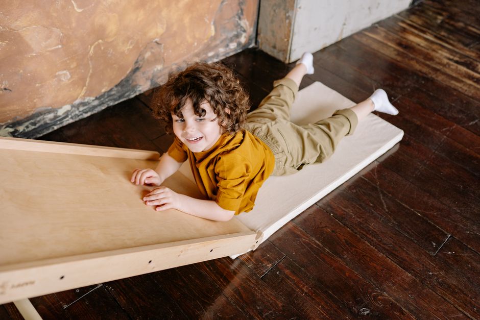 Curly-haired child smiling while playing on a slide indoors.