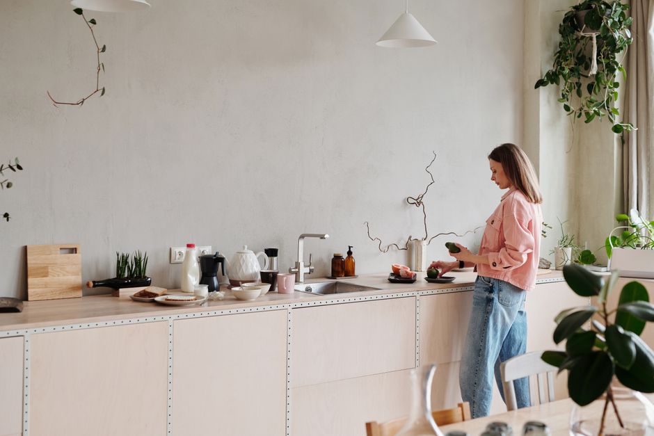 Woman slicing avocados on a stylish kitchen counter with plants around. Bright indoor setting.
