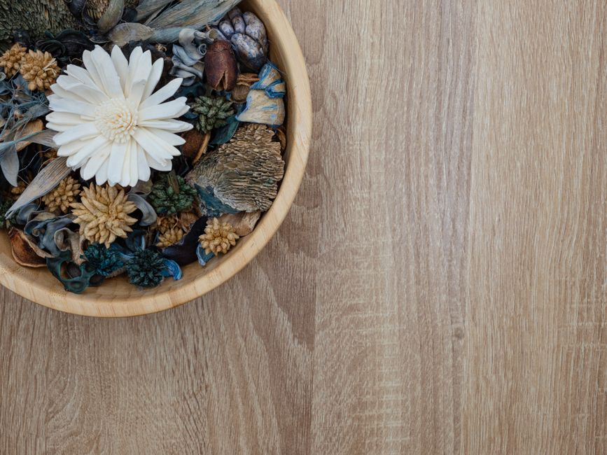 Top view of a wooden bowl filled with assorted decorative dried flowers on a wooden table.