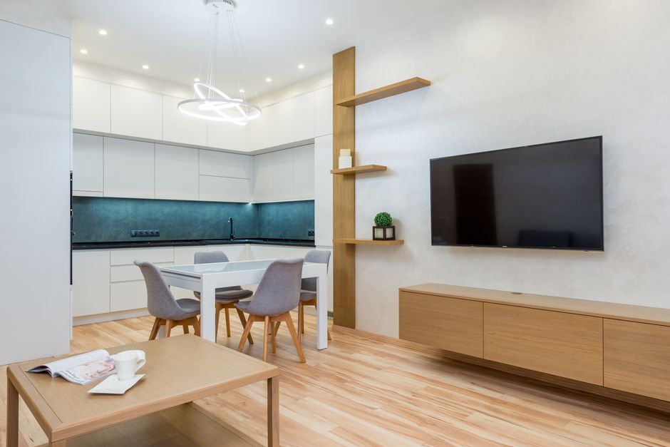 Modern apartment interior with open plan kitchen and living room with TV on wall and white cabinets