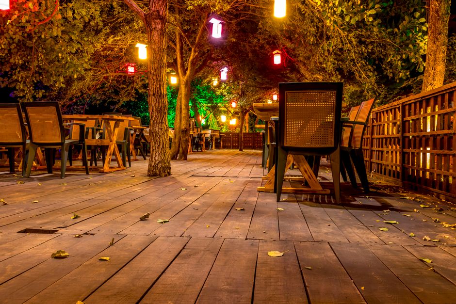 Charming outdoor dining setup with wooden tables and hanging lights, creating a warm and inviting atmosphere at night.