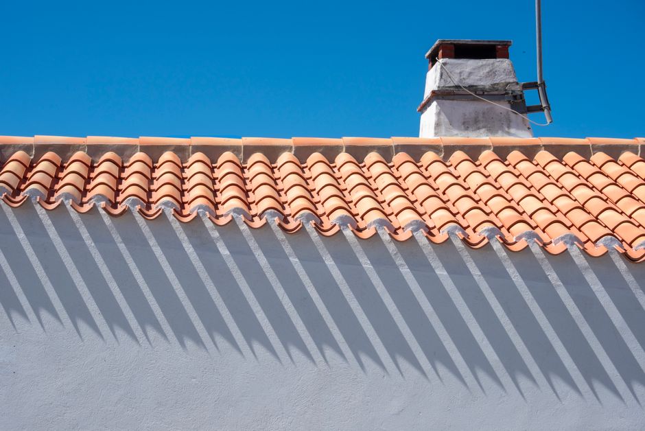 Orange roof tiles and chimney casting long shadows under a bright blue sky.