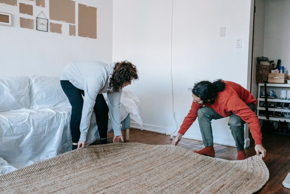 Couple arranging a rug in their contemporary apartment living room, teamwork concept.