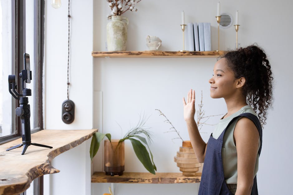 A young woman with curly hair vlogs indoors using a smartphone mounted on a tripod.