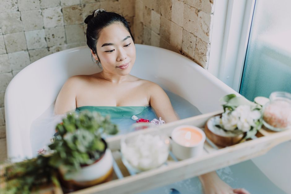 Woman enjoying a soothing bath with candles, flowers, and luxurious spa essentials indoors.