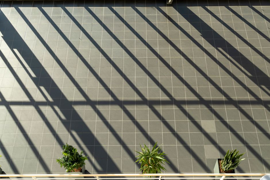 Sunlit shadows create patterns on a tiled balcony with potted plants, offering an artistic view.