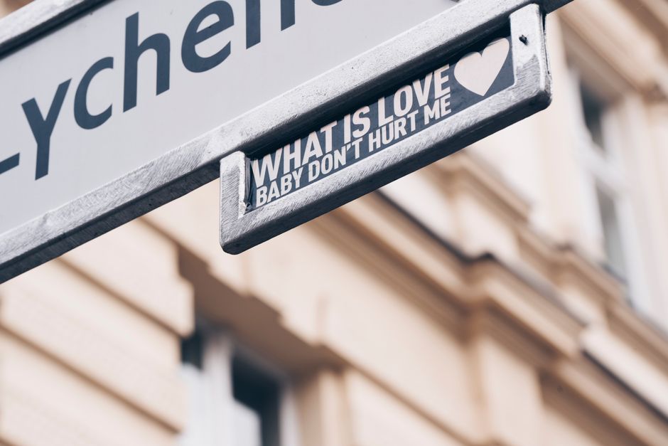 Street sign displaying 'What is Love' quote with heart icon in cityscape background.