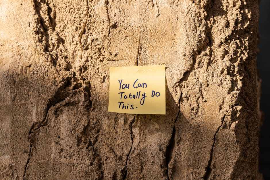 A sticky note with a motivational message on a textured wall in Dubai, with sunlight casting shadows.